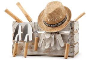 Image of a gardening hat, shovels, and other gardening tools propped up against a crate